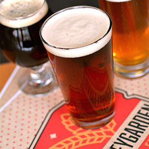 Three glasses of beer sit on a tabletop mat that reads 