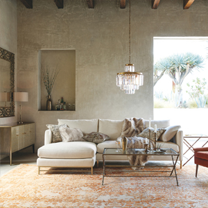 A cozy living room with a white sectional sofa and a glass coffee table adorned with decorative items, under a crystal chandelier, set against beige walls and large window