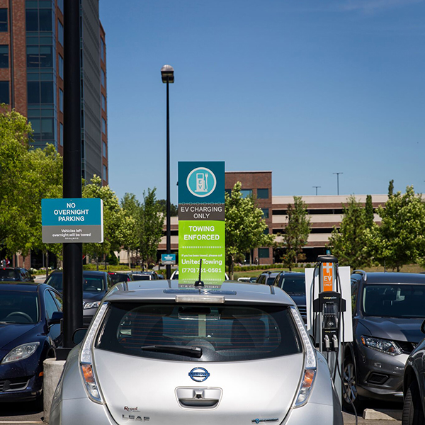 A silver electric car charges at an EV station within a parking lot