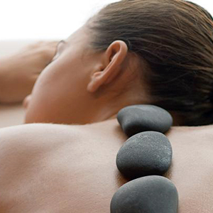 Dark stones rest along a person's back as they lie on their side, creating a calm and therapeutic atmosphere