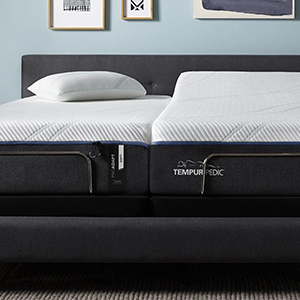 A split adjustable bed with Tempur-Pedic branding and white pillows is in a modern bedroom with blue walls and framed art on the wall above